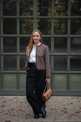 a lady in a white ruffle collared shirt, a brown jacket and a pair of black pants